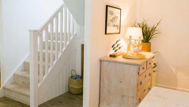 A staircase with white railings and a wooden floor, a small basket, and a cabinet with drawers and a lamp. - Ysgubor Wennol (Swallow Barn) -  a cosy fire that sleeps 4 guests  in 2 bedrooms (Llanfairpwll)