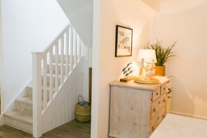 Eine Treppe mit weißen Geländern und Holzboden, ein kleiner Korb sowie ein Schrank mit Schubladen und einer Lampe.