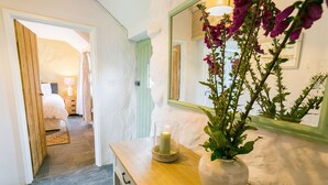 A hallway with a wooden door leading to a bedroom, a mirror on the wall, and a vase with flowers on a table. - Bryn Eithin -  a remote that sleeps 2 guests  in 1 bedroom (Bodorgan)