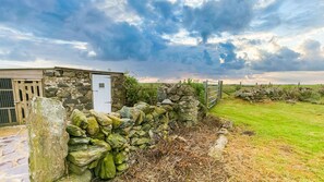 Un bâtiment en pierre avec une porte blanche, entouré d’un mur de pierre et d’un champ herbeux.