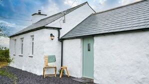 A white building with a green door, a wooden chair, and a small table. - Bryn Eithin -  a remote that sleeps 2 guests  in 1 bedroom (Bodorgan)