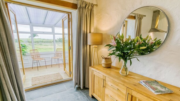 A room with a wooden cabinet, a mirror, a vase with flowers, a lamp, and a view of the outdoors through a glass door. - Bryn Eithin -  a remote that sleeps 2 guests  in 1 bedroom (Bodorgan)