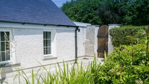 Une maison blanche avec un toit foncé, une porte en bois et une fenêtre avec des volets.