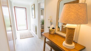 A hallway with a wooden bench, a mirror, and a lamp. There is a door at the end of the hallway. - Tideaway -  a coastal that sleeps 4 guests  in 2 bedrooms (Trearddur Bay)