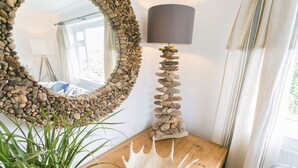 A room with a round mirror, a lamp with a stone base, and a wooden table with a plant. - Tideaway -  a coastal that sleeps 4 guests  in 2 bedrooms (Trearddur Bay)