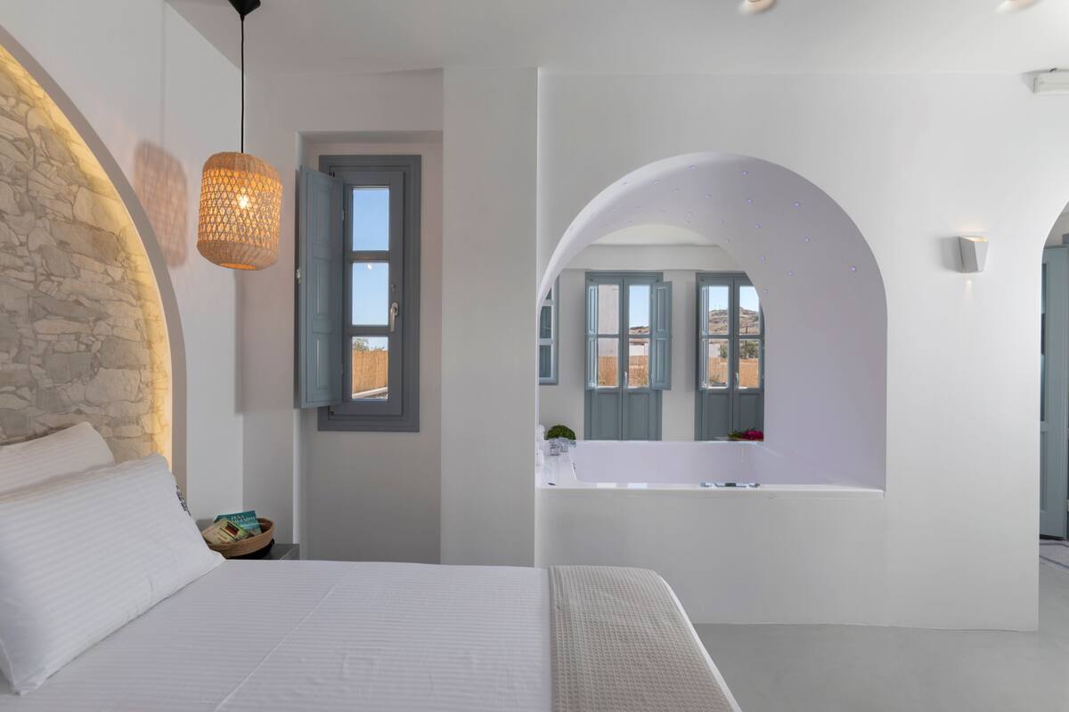A modern bedroom with a large bed, a stone accent wall, a hanging light fixture, and a view of the outside through a window.