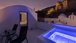 A modern rooftop terrace with a jacuzzi, a dining table with chairs, and a view of a historic building. - BlackStone Luxury Suites (Santorini)