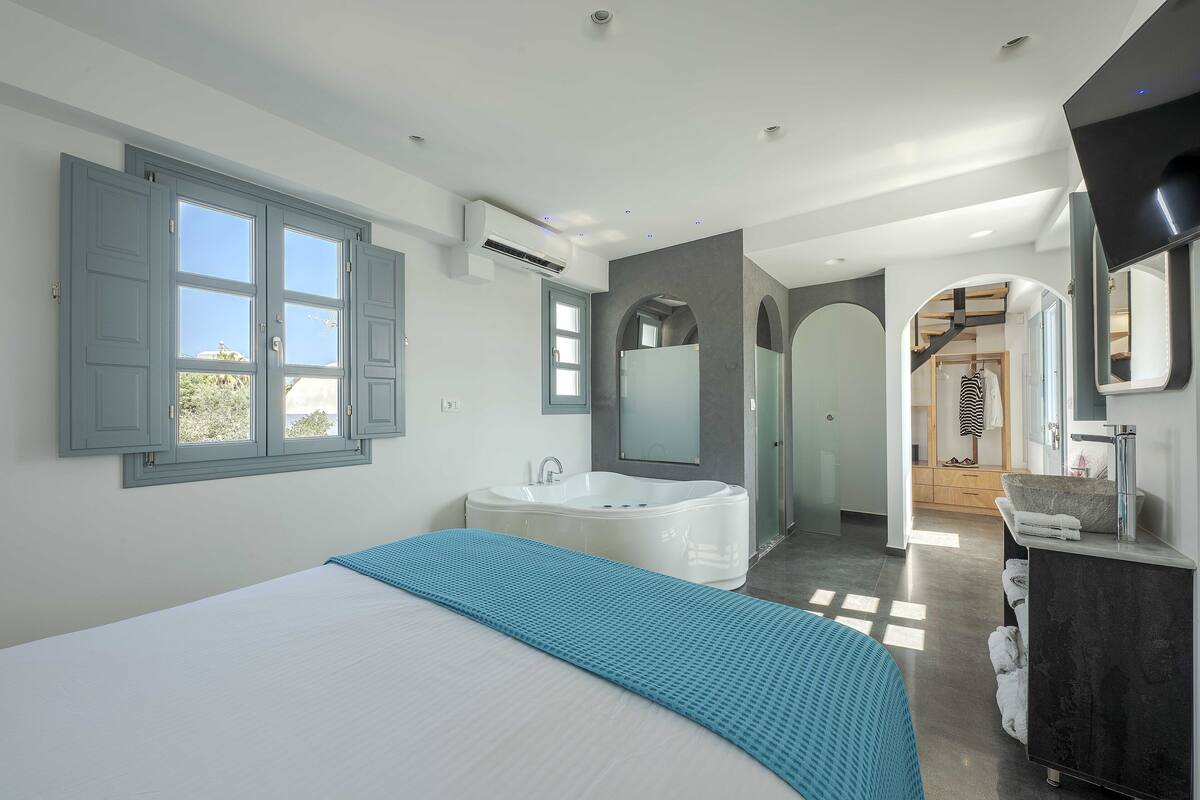 A modern bedroom with a large bed, a bathtub, and a walk-in closet.