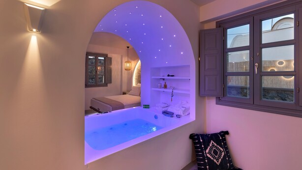 A modern bathroom with a freestanding bathtub, a vanity with a mirror, and a window with shutters. - BlackStone Luxury Suites (Santorini)