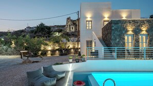 A modern building with a swimming pool, outdoor seating, and a stone wall. - BlackStone Luxury Suites (Santorini)