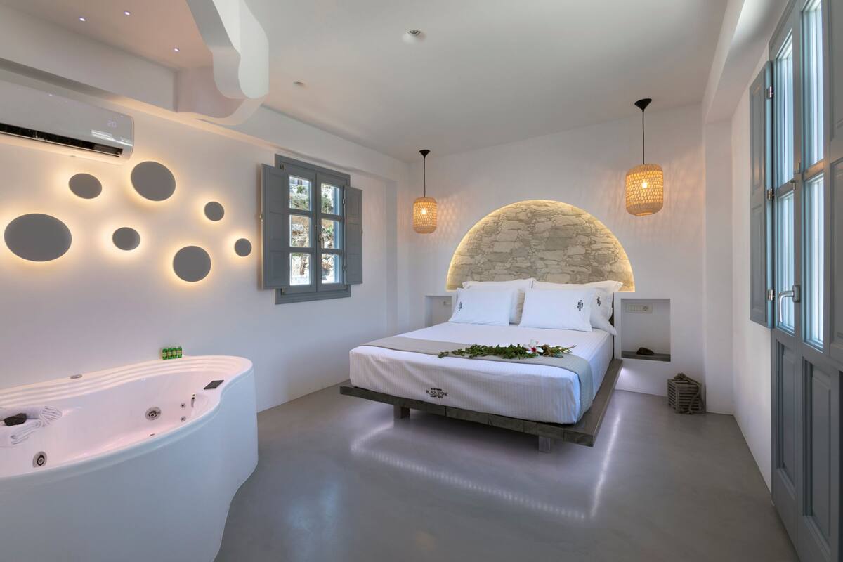 A modern bedroom with a large bed, a built-in bathtub, and a stone accent wall.