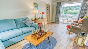 Ein Wohnzimmer mit einer Couch, einem Couchtisch mit Getränken, einem Sessel und Seeblick durch das Fenster.