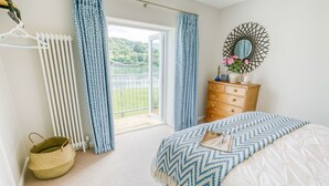 Ein Schlafzimmer mit Bett, Kommode, Spiegel und Blick auf einen See durch ein großes Fenster.