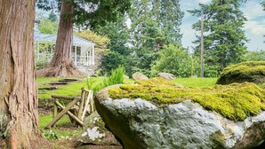 Un jardin rustique avec un grand arbre, une clôture en bois et un rocher recouvert de mousse.