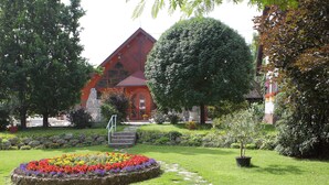 A garden with a stone pathway leading to a building with a red roof. - Ágnes Hotel (Hévíz)