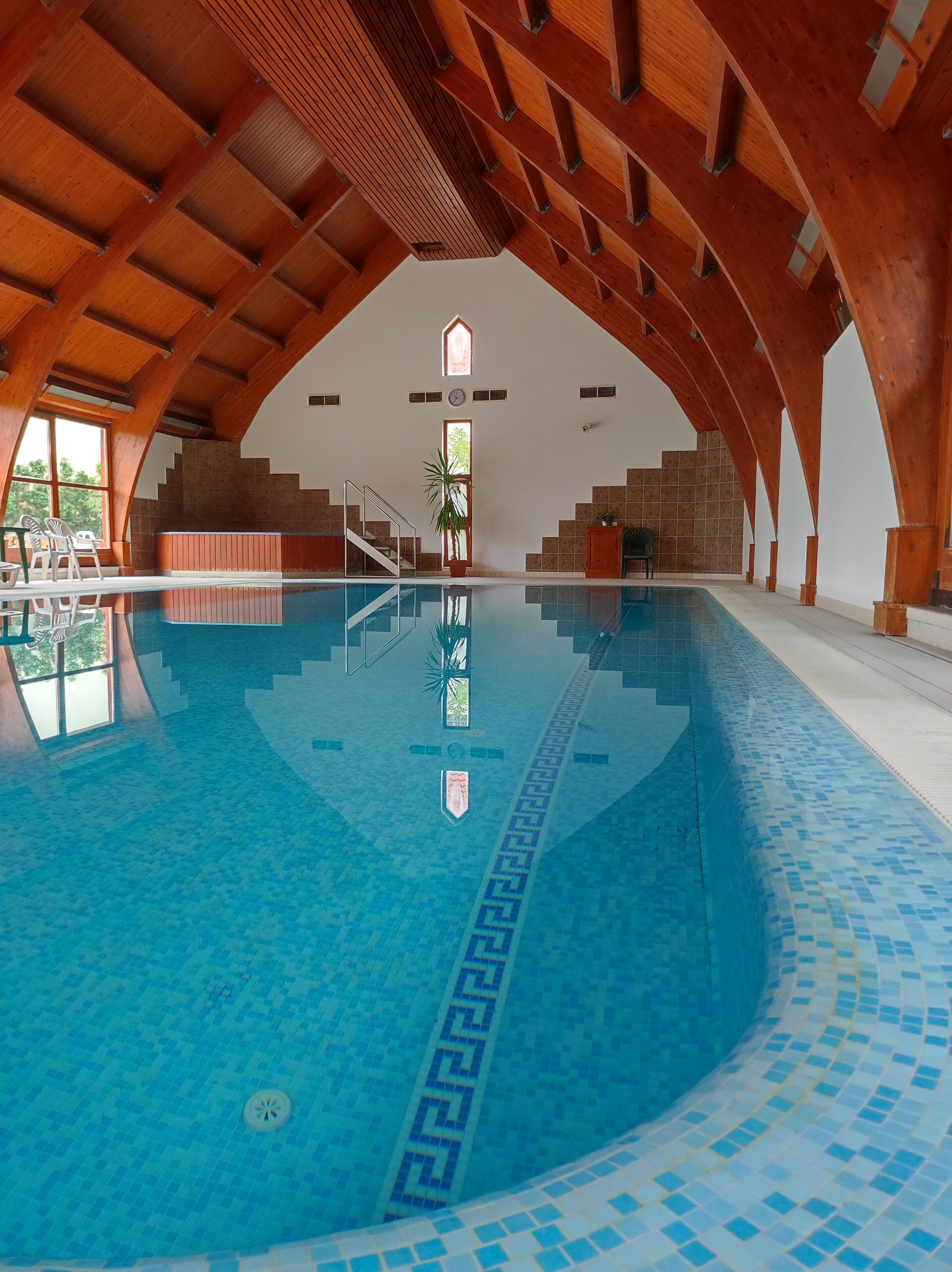 An indoor swimming pool with a tiled floor and wooden beams on the ceiling.