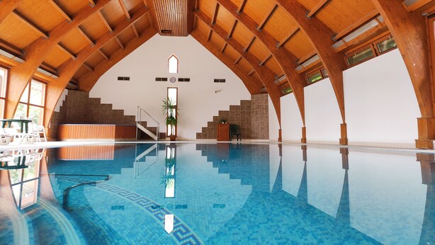 An indoor swimming pool with a high wooden ceiling and a tiled floor. - Ágnes Hotel (Hévíz)