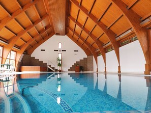 Una piscina interior con techo de madera alto y suelo de baldosas.