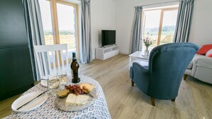 A living room with a dining table set for a meal, a TV, and a view of the outdoors. - Bwncath & Hebog -  a coastal that sleeps 8 guests  in 4 bedrooms (Llanfairynghornwy)