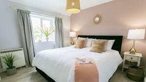 Siististi järjestetty makuuhuone, jossa on suuri sänky, yöpöytävalaisimet, koristeellinen peili ja ikkuna, jossa on verhot.