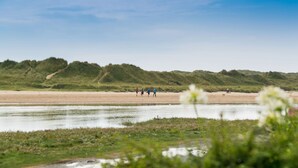 A beach with people walking, a sandy shore, and grassy dunes in the background. - Min y Don -  an on the beach that sleeps 4 guests  in 2 bedrooms (Aberffraw)