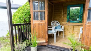 A wooden cabin with a porch, two white plastic chairs, and a small table with a cushion. - Borth Bach -  an on the beach that sleeps 4 guests  in 2 bedrooms (Rhosneigr)