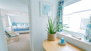 A bedroom with a bed, a chair, a potted plant, and a table with a candle. - Borth Bach -  an on the beach that sleeps 4 guests  in 2 bedrooms (Rhosneigr)