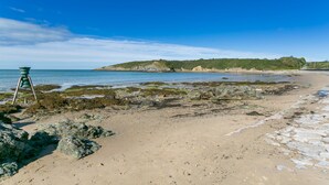Ein Strand mit felsigen Ufern, blauem Himmel und sanften Hügeln in der Ferne.