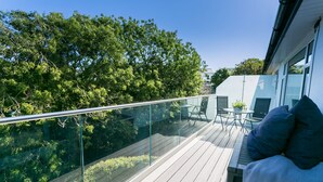 Ein Balkon mit Glasgeländer, Gartenmöbeln und Blick auf Bäume und ein Gebäude.