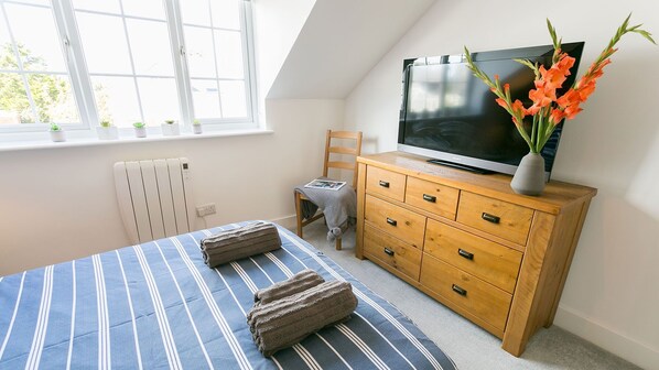 Un dormitorio con una cama, un aparador de madera, un televisor y una ventana con plantas.