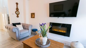 Un salon avec un canapé gris, une table basse ornée d’un vase de fleurs, un téléviseur à écran plat et une cheminée.