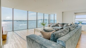 Un salon spacieux avec un grand canapé gris, une table basse et une vue sur l’eau.