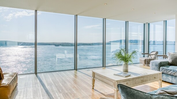 Un vaste espace de vie doté de grandes fenêtres offrant une vue sur l’eau et le paysage lointain.