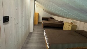 Een compacte kamer met schuin dak, twee bedden, een houten garderobe en een klein kastje.