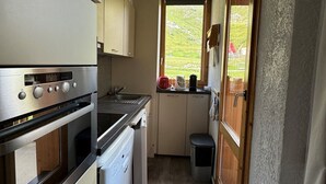 Een compacte keuken met een kookplaat, oven en vaatwasser, een klein spoelgedeelte en een raam met uitzicht op een groen landschap.