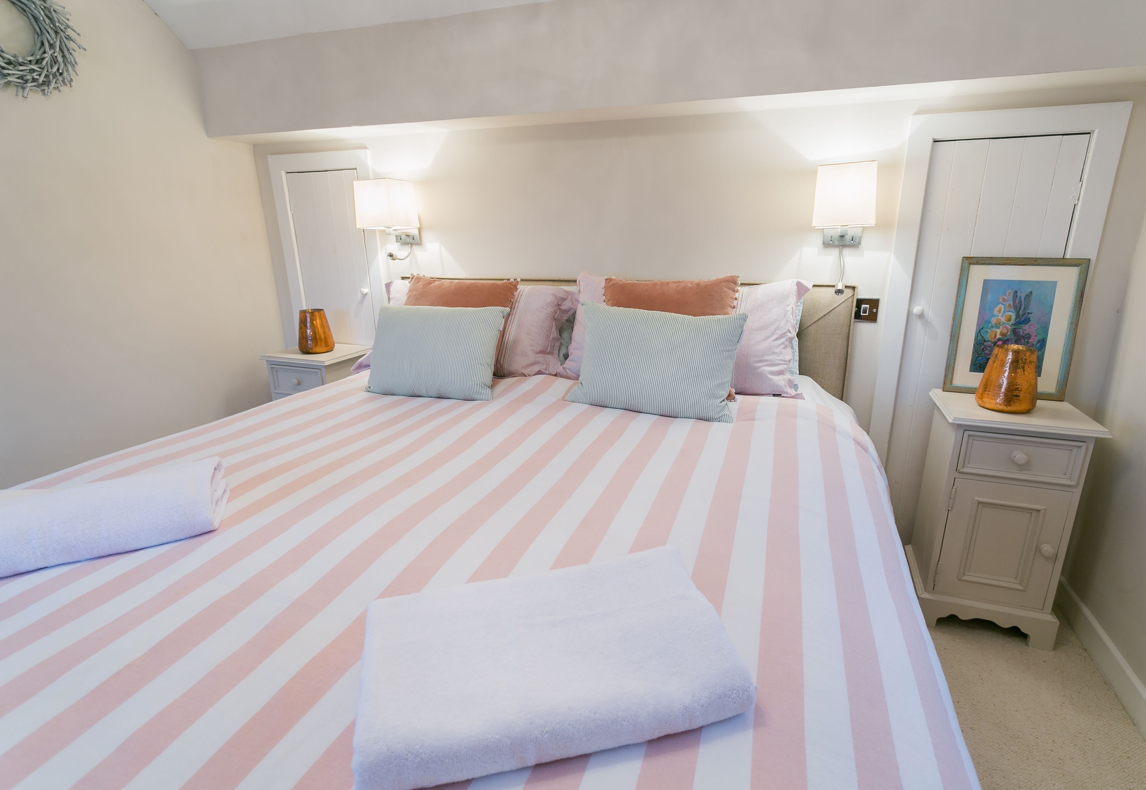 A neatly made bed with striped bedding and pillows, bedside tables with lamps, and a framed picture on the wall.