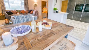 A modern living room with a wooden coffee table, a sofa, and a dining area with a plate of cheese and grapes.