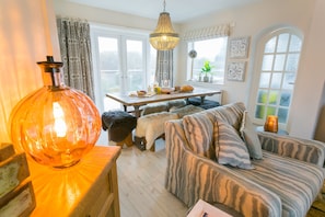 A cozy living room with a large wooden table, a sofa, and a hanging light fixture. - Coed Helyg -  a coastal that sleeps 14 guests  in 7 bedrooms (Abersoch)