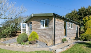 A small wooden cabin with a gabled roof, a front door, and a window. - Easter Cabin -  a remote that sleeps 4 guests  in 2 bedrooms (Moelfre)