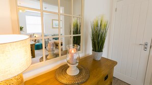 Een houten tafel met een kaars in een glazen houder, een geweven onderzetter en een potplant.