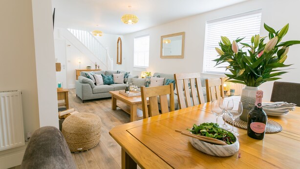 Een eetgedeelte met een houten tafel, stoelen, een saladeschaal, een fles wijn en een potplant.