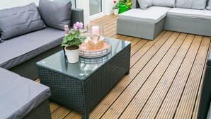 Een overdekte buitenruimte met rieten meubels en een tafel met glazen blad.