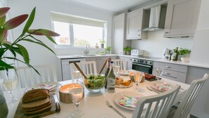 Een moderne keuken met witte kastjes, een eettafel gedekt voor vier personen, en diverse etens- en drankjes.