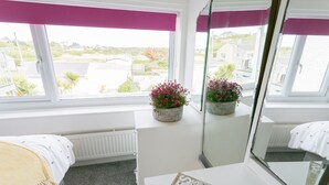 Een hotelkamer met twee bedden, een groot raam met uitzicht op zee en een tijdschrift op de tafel.
