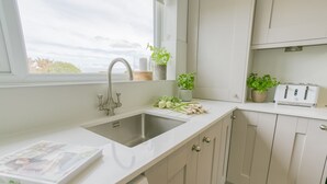 Een moderne keuken met een roestvrijstalen spoelbak, witte kasten en een raam met uitzicht op de lucht.