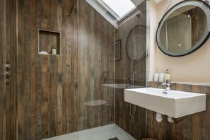 A modern bathroom with a wooden wall, a glass shower enclosure, a white sink, and a round mirror. - Glandwr -  an on the beach that sleeps 7 guests  in 3 bedrooms (Rhosneigr)