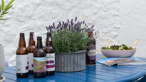 A table with bottles of beverages, a potted lavender plant, a bowl of salad, and a magazine. - Gwyndy -  a town that sleeps 4 guests  in 2 bedrooms (Beaumaris)