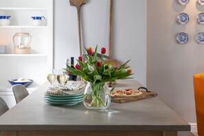 Una mesa de comedor con un jarrón de tulipanes, platos, vasos y una pizza sobre una tabla de cortar.