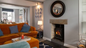 A cozy living room with a fireplace, a sofa, a lamp, and decorative plates on the wall. - Gwyndy -  a town that sleeps 4 guests  in 2 bedrooms (Beaumaris)