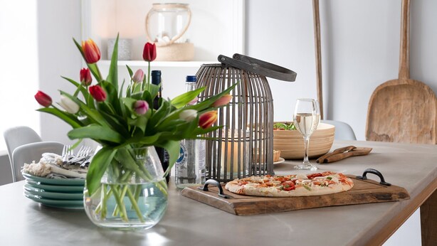 A dining table with a pizza, a vase of tulips, a candle, and a glass of water. - Gwyndy -  a town that sleeps 4 guests  in 2 bedrooms (Beaumaris)